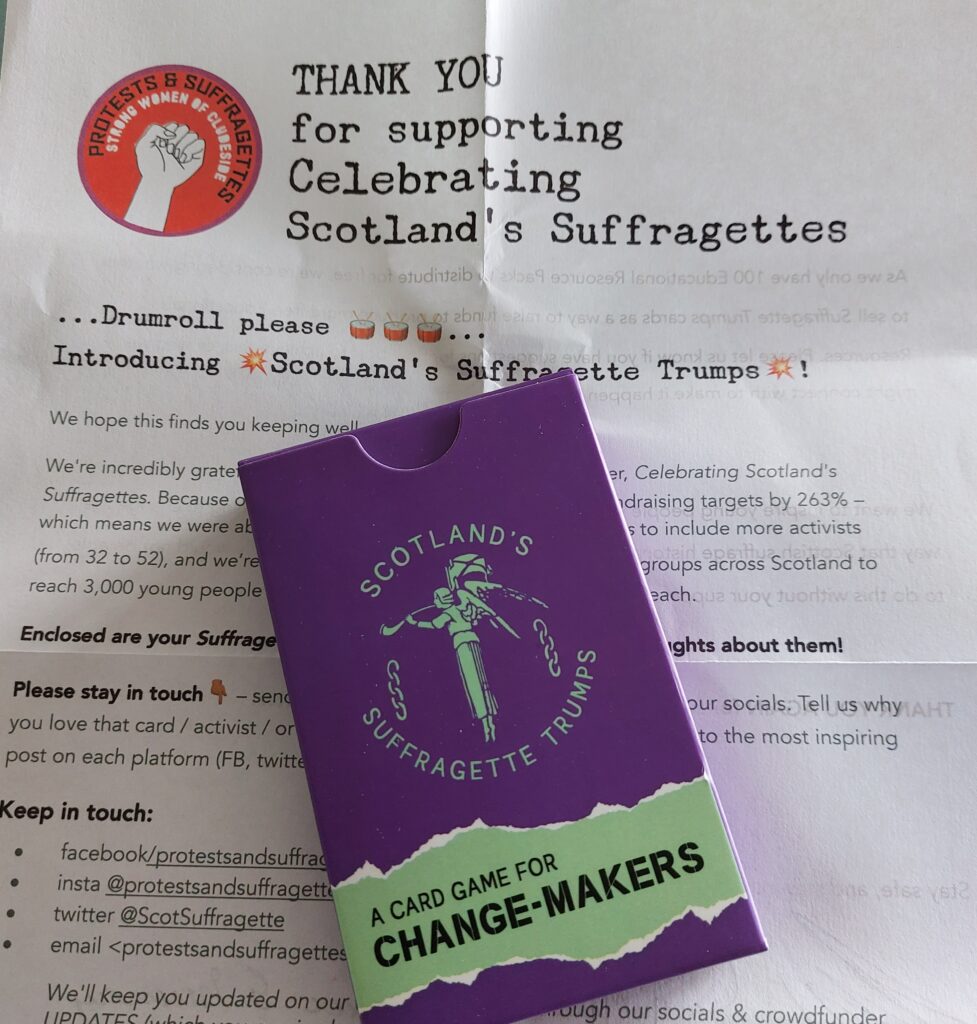 A pack of cards with text Scotland's Suffragette Trumps, a card game for change-makers. The pack is in the suffragette colours of purple and green, against a background of a letter from Protests and Suffragettes with their contact information on it.
