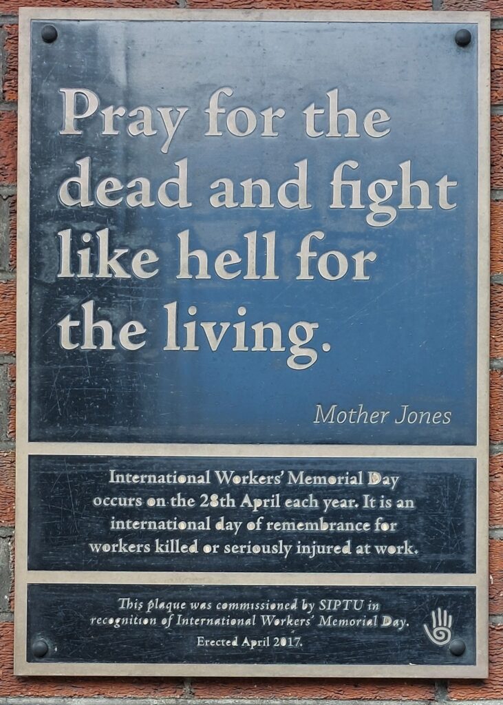 Black rectangular plaque on brick wall.  Text reads “Pray for the dead and fight like hell for the living”. Mother Jones. International Workers' Memorial Day occurs on the 28th April each year, It is a day of remembrance for workers killed or seriously injured at work. Erected by SIPTU, April 2017.