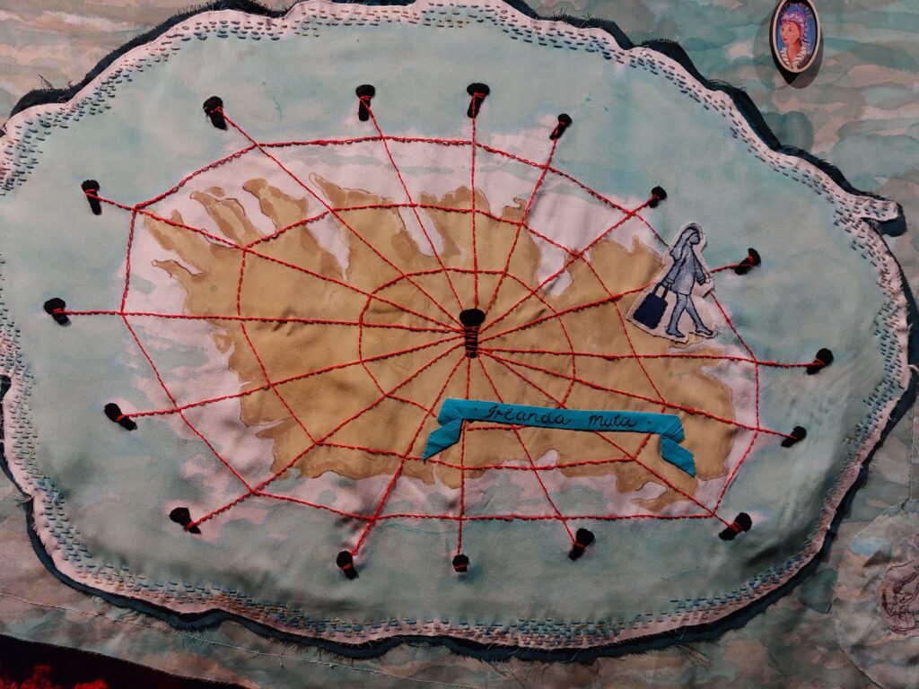 EMbroidered panel of an island with a net or web of wool on top of it. A figure of a woman with a suitcase is leaving the island