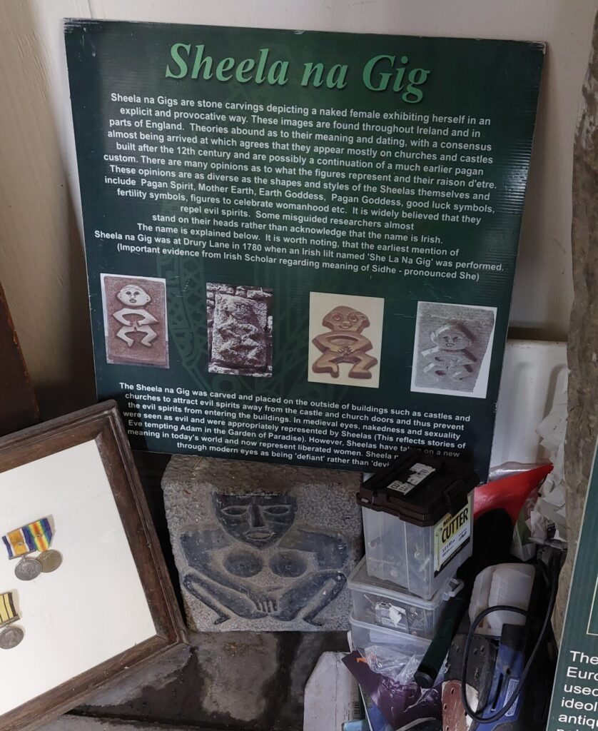 A replica Sheela na Gig figure surrounded by memorabilia in Cashel Folk Village