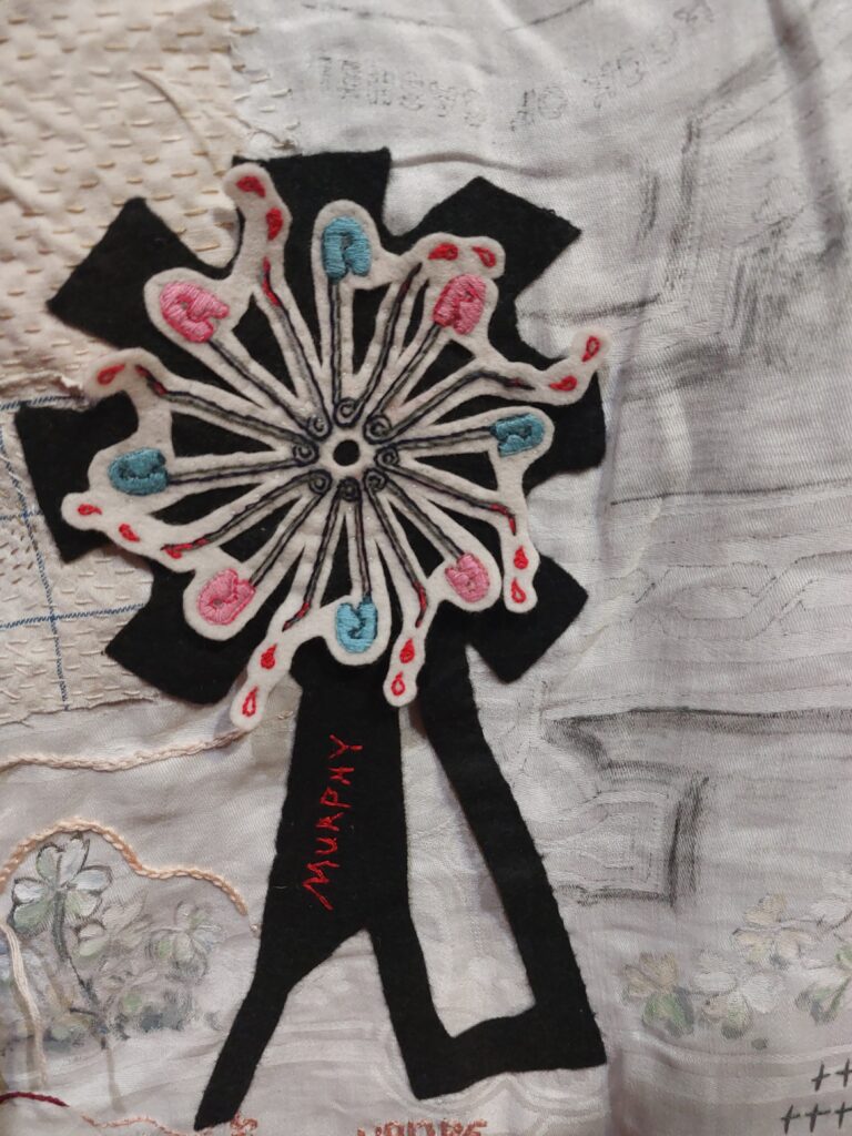 A circle of embroidered safety pins with drops of blood and the name Murphy on fabric, a detail from The Map by artists Alice Maher and Rachel Fallon