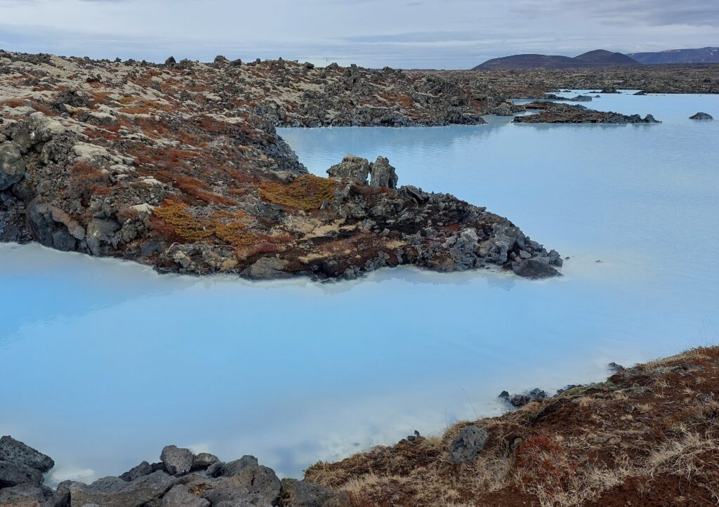 Part of the blue lagoon in Iceland. The water is a milky blue colour and is surrounded by volcanic rock.