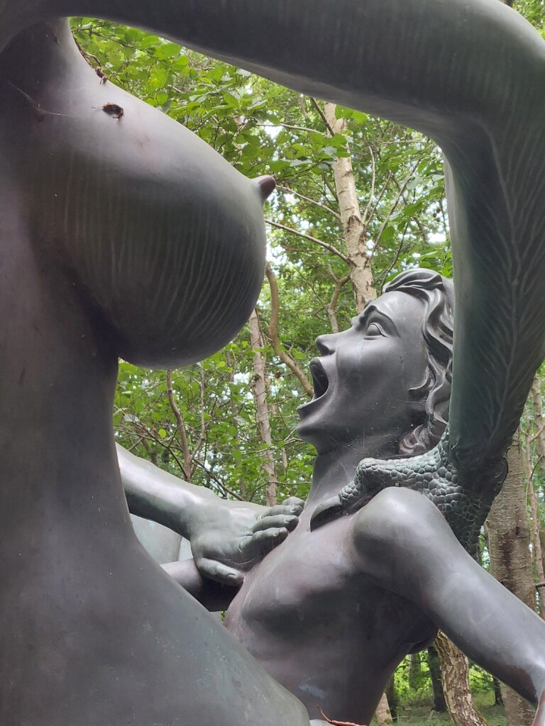 A sculpture of a female figure holding a child with gaping mouth near a large breast