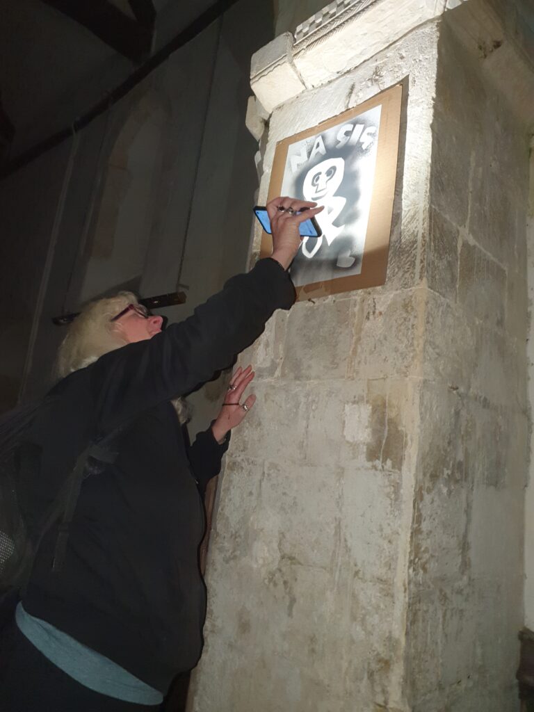 Woman attaching a spray-painting of a Sheela na Gig figure to a wall. 