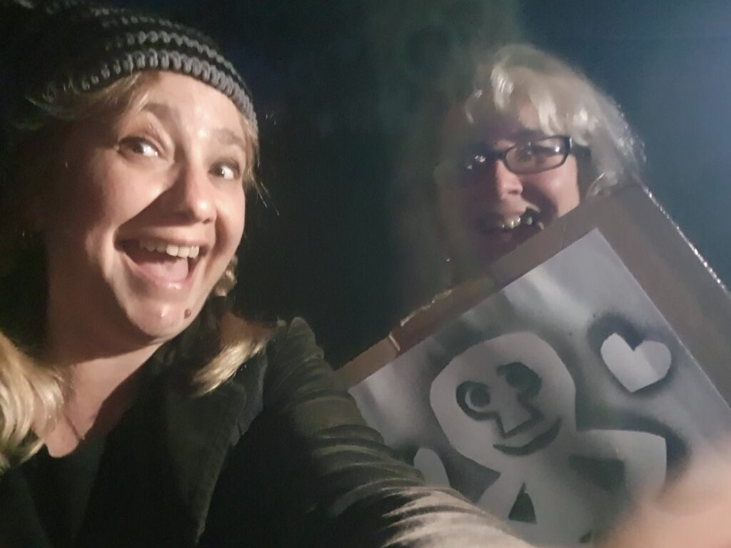 two women with a spray painting of a Sheela na Gig figure.